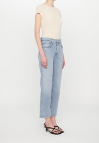 Top beige de manga corta con textura de canalé, jeans de pierna recta azul claro, sandalias negras de tiras. Tejido suave, corte relajado y estilo clásico de denim.