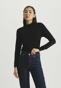 Haut noir à col roulé à manches longues en tissu extensible, associé à un jean en denim foncé taille haute doté de poches avant et d'une fermeture à bouton.
