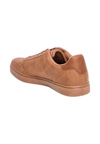 Zapatilla de ante color arena con punta redondeada, suela de goma plana y costuras tonales. El talón presenta un acento de cuero marrón contrastante.