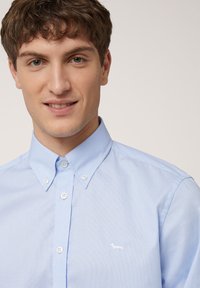 Lichtblauw overhem shirt met een gestructureerd patroon, zachte stof en een klein wit hondenlogo op de linkerborst; klassieke kraagontwerp.