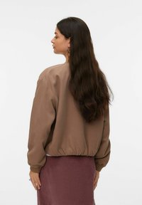 Sweat-shirt marron court à manches longues, avec des poignets côtelés et une texture lisse, associé à une jupe en velours côtelé bordeaux. Vue de dos.