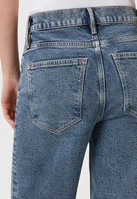 Jeans in denim azzurro chiaro con vita alta, due tasche posteriori e cuciture a contrasto. Il tessuto presenta una texture leggermente sbiadita.