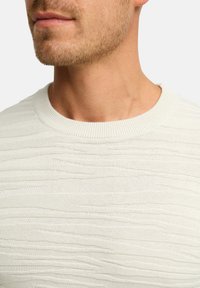 Maglione grigio chiaro con un motivo testurizzato a onde e un colletto a girocollo a coste. La vista ravvicinata mette in evidenza i dettagli e la texture del tessuto.