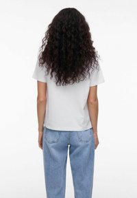 Hvid t-shirt med korte ærmer og en afslappet pasform, parret med lyseblå højtaljede denimjeans, der har opbrettede manchetter og syede lommer.