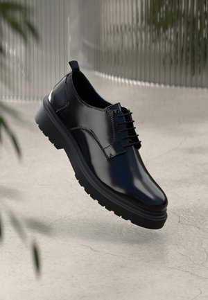 Schwarzer Lederschuh mit glänzender Oberfläche, runder Spitze, Schnürdesign, kontrastierenden Nähten und einer dicken Gummisohle mit Profilmuster.