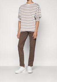 Koszula w paski z długim rękawem w kolorze białym i jasnobrązowym, zestawiona z brązowymi spodniami i białymi trampkami. Prosty krój, luźne dopasowanie. Brak wyróżniających się wzorów.