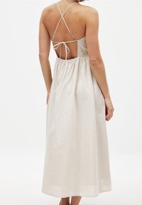 Robe en lin beige à coupe mi-longue, dos ouvert, bretelles croisées et taille froncée pour un ajustement décontracté. Texture lisse et légère.