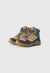 Hiking boots featuring a mix of tan, teal, and orange colors, a rubber sole, textured material, and three white stripes on the side.