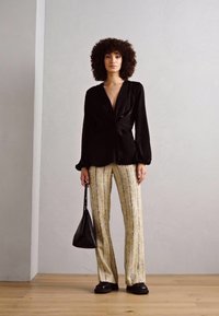 Svart blus med lång ärm och knutdetalj, matchad med randiga byxor i gult och grått med vida ben. Accessoarer inkluderar en liten svart väska och klumpiga skor.