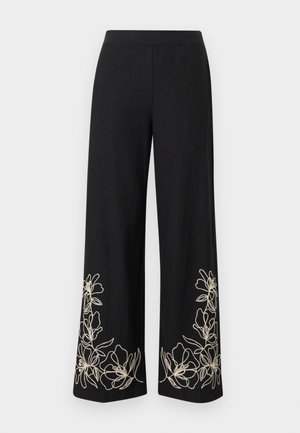 Pantaloni neri a gamba larga con ricamo floreale beige lungo gli orli inferiori su uno sfondo chiaro e semplice.