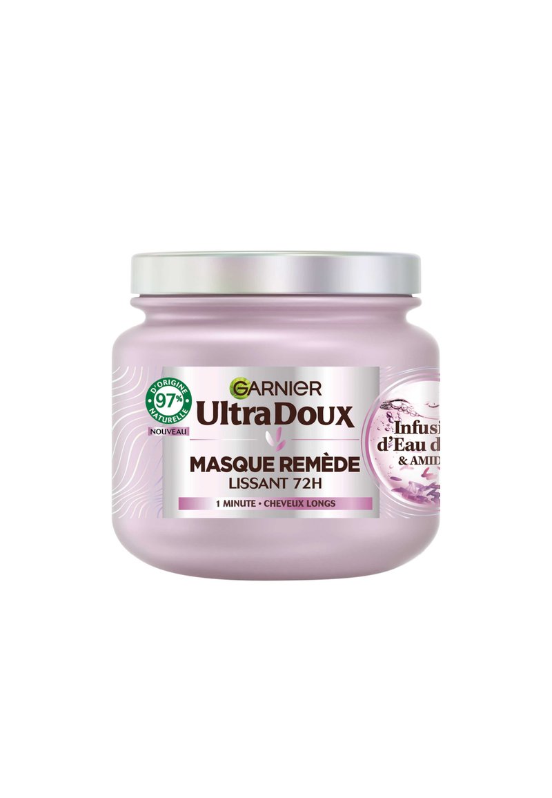 Bocal rond violet clair avec un couvercle en argent, présentant une étiquette blanche affichant le nom du produit et les détails en texte noir, accents graphiques floraux.