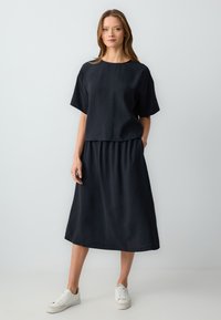 Completo due pezzi nero composto da una maglietta ampia a maniche corte e una gonna dal taglio al ginocchio, realizzato in un tessuto morbido e leggero.