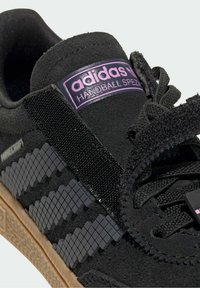Sneaker in suede nero con dettagli neri testurizzati, marchio viola e design pixelato. Presenta una suola in gomma color gomma e chiusura con lacci.