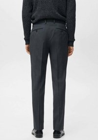 Szare, dopasowane spodnie o gładkiej fakturze, z dwoma tylnymi kieszeniami i subtelnymi fałdami wzdłuż nóg. Noszone z ciemnym swetrem i butami.