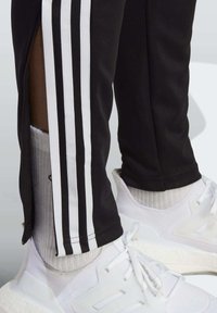 Svarta träningsoveraller med vita sidostråk, med en dragkedja vid fållen. Matchas med vita sneakers och ljusgrå strumpor.