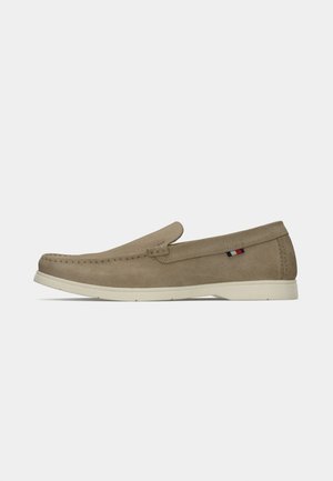 Beige suede slip-on shoe with classic moccasin stitching, flat white rubber sole, and a small accent detail in red, white, and blue.