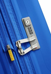 Valigia blu con superficie testurizzata, tiretti in metallo argentato e lucchetto approvato TSA con tastierino numerico. Logo Delsey in giallo.