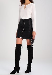 Valkoinen pitkähiha тоҷик, jossa on avainreikät yksityiskohtana, yhdistetty mustaan nahkahameeseen, jossa on etuvetoketju ja hopeiset yksityiskohdat. Polviin asti ulottuvat mustat saappaat.