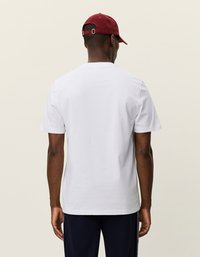 Λευκό βαμβακερό t-shirt με στρογγυλή λαιμόκοψη, κοντά μανίκια και χαλαρή εφαρμογή, συνδυασμένο με ένα κόκκινο καπέλο. Απλός σχεδιασμός, χωρίς σχέδια ή γραφικά.