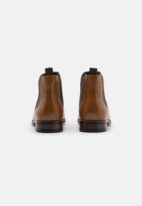 Brązowe skórzane botki za kostkę z elastycznymi panelami bocznymi, zaokrąglonym noskiem i kontrastowym ciemnobrązowym obcasem; gładka faktura i przeszycia.