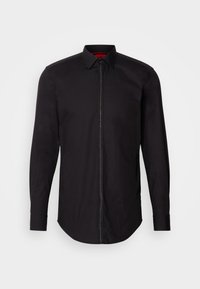 Chemise homme noire à manches longues avec col et fermeture éclair centrale sur fond blanc, coupe cintrée et poignets boutonnés.