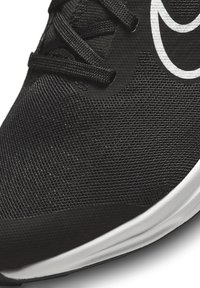 Schwarzer Sportschuh mit einem strukturierten Mesh-Obermaterial, weißem Logo und einer strapazierfähigen Gummisohle, ausgestattet mit Schnürsenkeln für einen sicheren Halt.