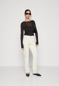 Top negro de manga larga, cuello en forma de U, vaqueros blancos de pierna recta, zapatos negros sin cordones y gafas de sol rectangulares; diseño minimalista.
