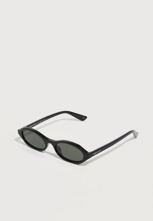 Black oval sunglasses with dark lenses and slim arms, branded "McQueen" on the temple, resting on a white surface.
