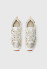 Witte en beige sneakers met gaaspanelen en metalen accenten. Voorzien van veter, gevoerd kraag en een rubberen zool met logodetail.