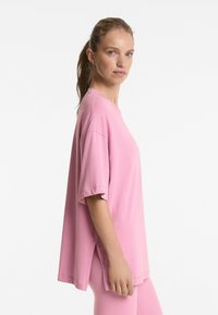 Tricou roz oversized cu mâneci scurte, având un guler rotund și slituri laterale pentru confort; fabricat dintr-un material moale și ușor.