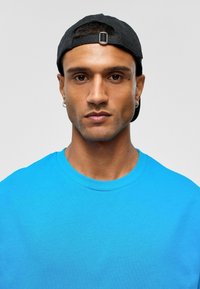 Heldere blauwe T-shirt met korte mouwen en een ronde hals; gedragen met een zwarte pet. Soepele textuur, minimalistisch ontwerp, geen patronen of accenten.