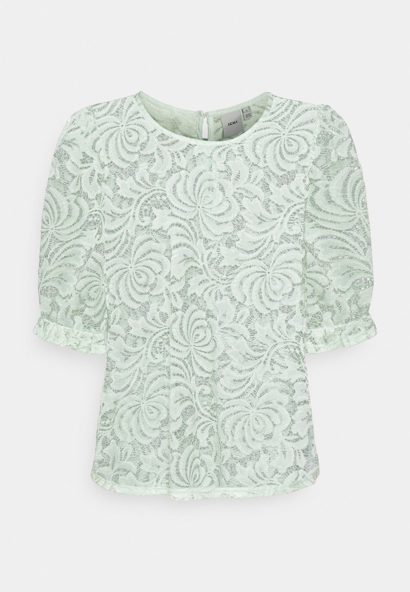 Blouse en dentelle vert clair avec motifs floraux, manches courtes bouffantes, col rond et fermeture par bouton goutte d'eau dans le dos.