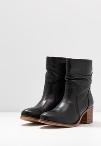 Bottines en cuir noir à cheville avec un design légèrement froissé, talon en bois empilé et détails cousus le long des coutures.