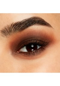 Nahaufnahme eines Auges mit warmem braunem Lidschatten, der sanft verblendet ist, dunklen Wimpern und einer gut definierten, natürlichen Augenbraue. Der Hautton ist hell.