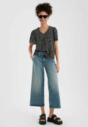 Zwart blouse met stippen en korte mouwen, gecombineerd met lichte spijkerbroek met wijde pijpen en zwarte platform sandalen. Soepele texturen, casual pasvorm.