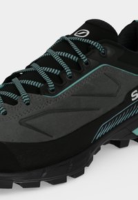 Gros plan d'une chaussure de randonnée grise et noire avec des accents bleu sarcelle et des lacets à motifs sur une semelle noire robuste.