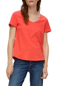 T-shirt met korte mouwen en v-hals in helder koraal, gemaakt van zachte stof met een ontspannen pasvorm en onafgewerkte zoomranden, gecombineerd met blauwe jeans.