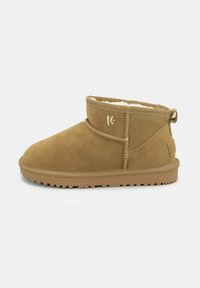 Stivaletti ankle in suede beige con una morbida fodera interna, punta arrotondata e suola in gomma. Presentano un anello sul retro e dettagli di cucitura discreti.