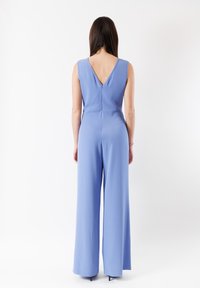 Giacca blu senza maniche con un design a V sulla schiena, gamba ampia, tessuto liscio e una chiusura a cerniera discreta sul retro.