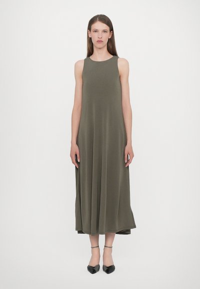 Vestido maxi sin mangas de color verde oliva, hecho de una tela suave, con una silueta relajada y un dobladillo recto. Zapatos negros de punta con correas en los tobillos.