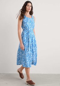 Rochie midi albastră și albă cu flori, cu un corset ajustat, decolteu rotund și talie legată. Asortată cu saboți maro slip-on. Textură a țesăturii netedă.