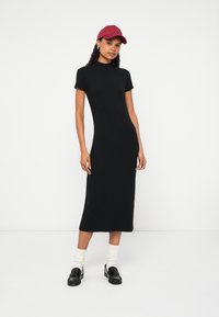 Melna ribota midi kleita ar īsām piedurknēm, augstu kaklu un gludu tekstūru. Kopā ar tumši sarkanu cepuri un melniem loaferiem, papildināta ar baltām zeķēm.