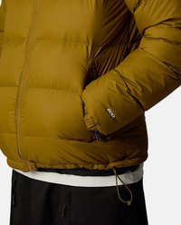 Giacca puffer gialla senape con texture imbottita, polsini elastici e tasche con zip. Presenta cordoncini sul bordo e logo del brand sulla manica.