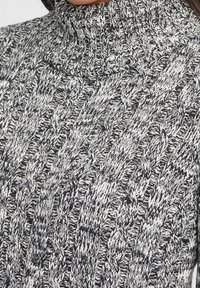 Pull à col roulé en tricot noir et blanc, présentant un motif en câbles texturé et une coupe ajustée autour du col.