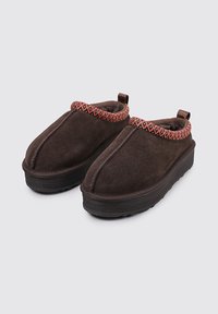 Zapatos de ante marrón tipo slip-on con una suela de goma negra texturizada y un borde colorido tejido en el cuello. Diseño de punta redondeada.