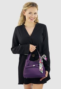 Paarse leren handtas met een gestructureerd oppervlak, voorzien van een kleurrijk patroon sjaal die om het handvat is geknoopt; gestructureerd ontwerp met dubbele banden.