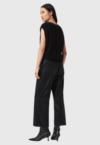 Top in maglia nera senza maniche, modello boxy, abbinato a pantaloni larghi neri brillanti e stivaletti con punta, fotografato da dietro.