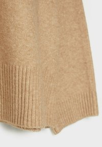 Tissu tricoté brun clair avec bords côtelés, montrant la texture et le matériau en laine douce.