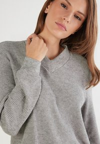Grauer gerippter Pullover mit V-Ausschnitt, langen Ärmeln und weicher Textur. Hat eine lässige Passform und dezente Nähte.