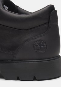 Schwarzer Lederstiefel mit strukturiertem Obermaterial, verstärkter Ferse, dicker Gummisohle und geprägtem Baum-Logo. 